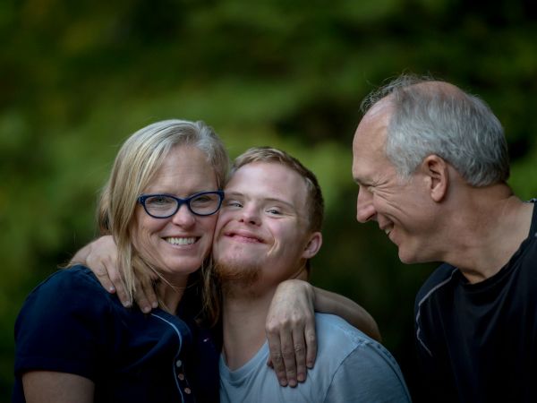 Padres abrazados con su hijo adulto