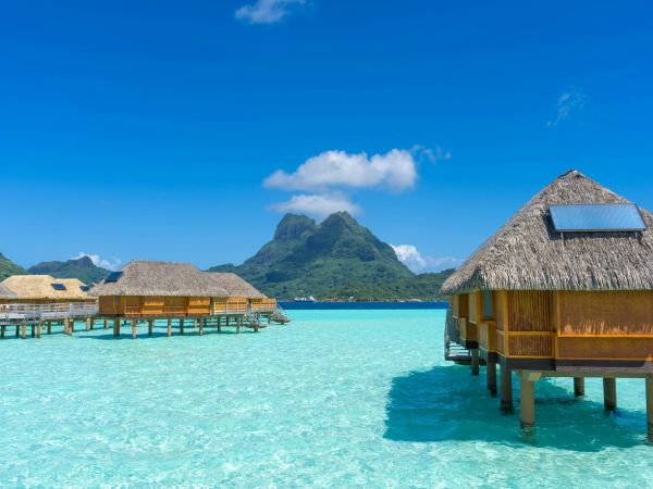 Bungalows con techo de paja sobre la laguna cristalina de Bora Bora, con el Monte Otemanu al fondo
