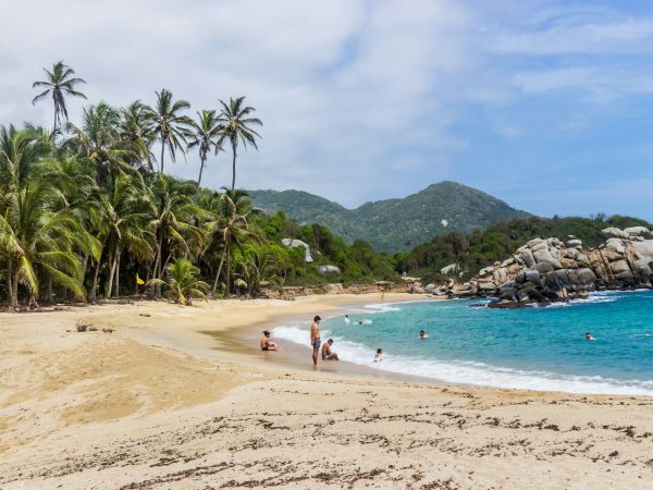 Playa de arena dorada con palmeras y grandes rocas en el Parque Nacional Tayrona, Colombia