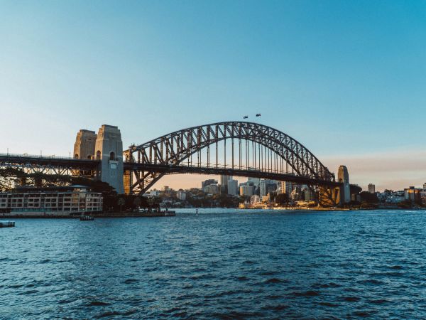 Puente de la Bahía de Sídney sobre las aguas del puerto, con los rascacielos del centro al atardecer, Australia