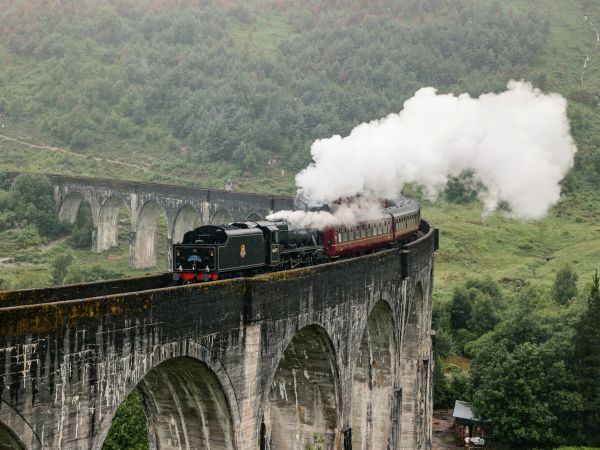 Tren de vapor cruzando el viaducto de Glenfinnan entre montañas verdes, Escocia