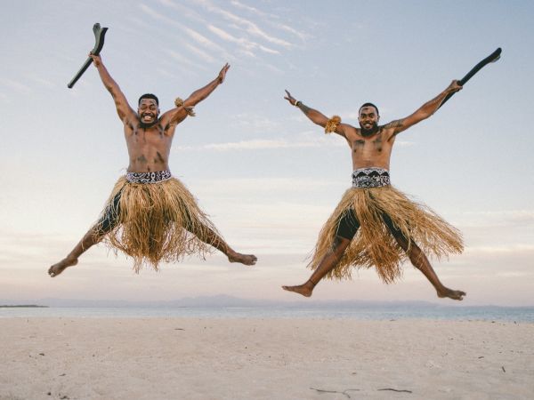 Dos guerreros fijianos con faldas de hierba saltando en la playa de Beachcomber Island, Fiji