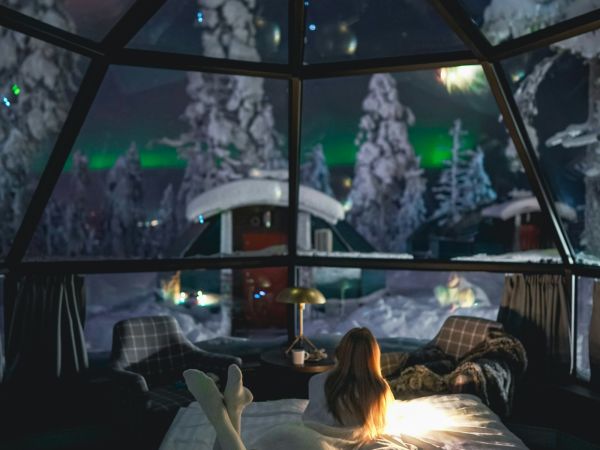 Vista desde la cama de un iglú de cristal con aurora boreal sobre el bosque nevado, Levi, Laponia finlandesa