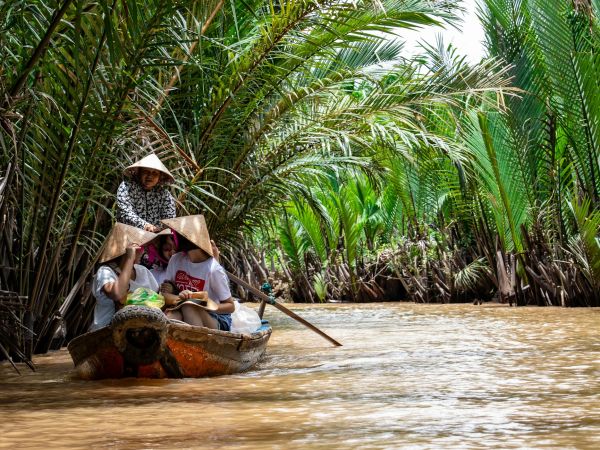 Barca de remos con sombreros cónicos en un canal bordeado de palmeras, delta del Mekong