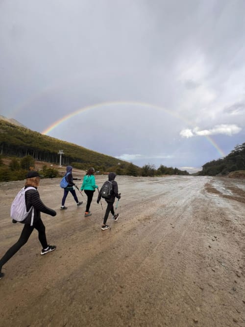 Personas caminando en un sendero mojado por la lluvia con un arcoiris en el paisaje