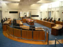 The empty debating chamber of the ACT Legislative Assembly in Canberra, with curved timber benches and flags behind the Speaker's chair
