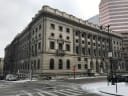 The Clarence M. Mitchell Jr. Courthouse in downtown Baltimore under a grey winter sky, with snow on the street corner in front