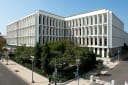 The Hart Senate Office Building on Capitol Hill in Washington, its white marble facade and rows of windows under a clear blue sky, with trees and a street corner in the foreground