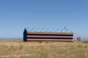 A barn painted as the American flag stands in dry grassland outside Madera, California, under a clear blue sky