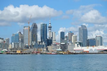 Auckland's city centre skyline and the Sky Tower seen across the Waitemata Harbour under a blue sky with cumulus cloud