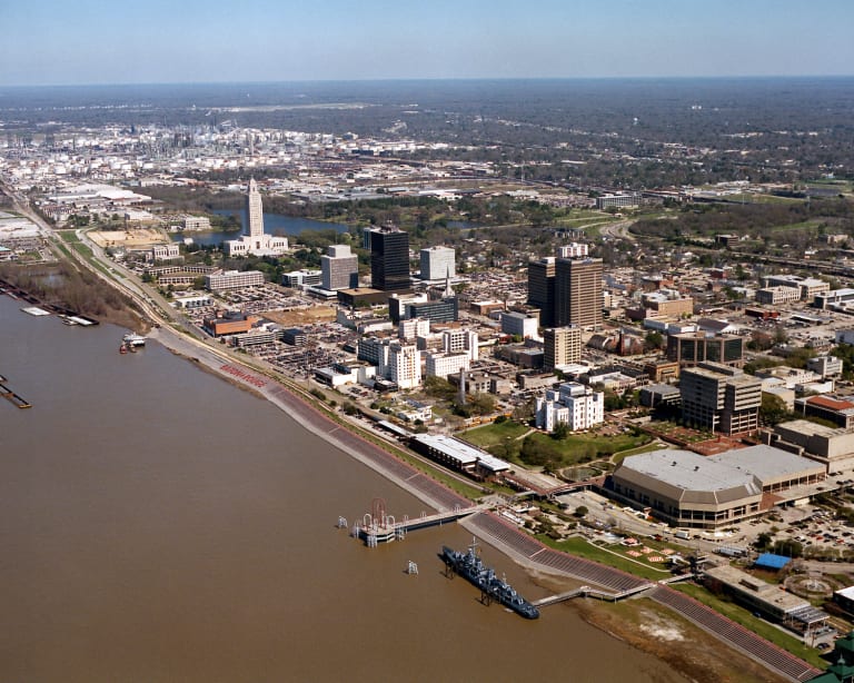 Aerial view of downtown Baton Rouge beside the Mississippi River, with the Louisiana State Capitol tower in the distance