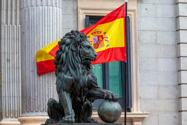 A bronze lion outside the Congreso de los Diputados in Madrid with the Spanish flag flying behind