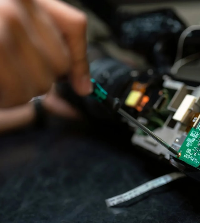 Technician working on a device circuit board with tools at a repair bench
