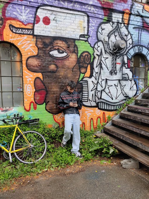 Street art mural in Christiania, Copenhagen with a colorful painted face, a bicycle, and a person standing nearby