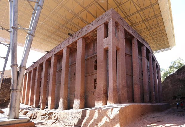 "Exterior view of the massive Biete Medhane Alem church, carved from solid rock with thirty-four columns, protected by a modern metal canopy in Lalibela."