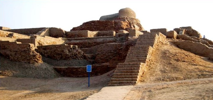 "Ancient ruins of Mohenjo-Daro with a large brick staircase leading up the citadel mound to a domed Buddhist stupa under a clear sky in Pakistan."