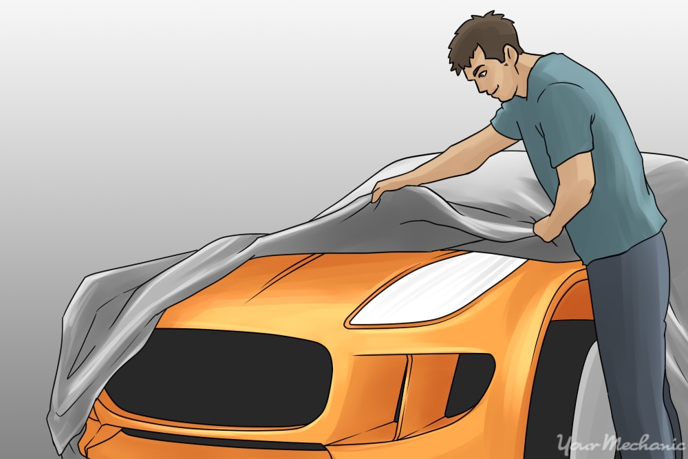 man placing a car cover on a vehicle