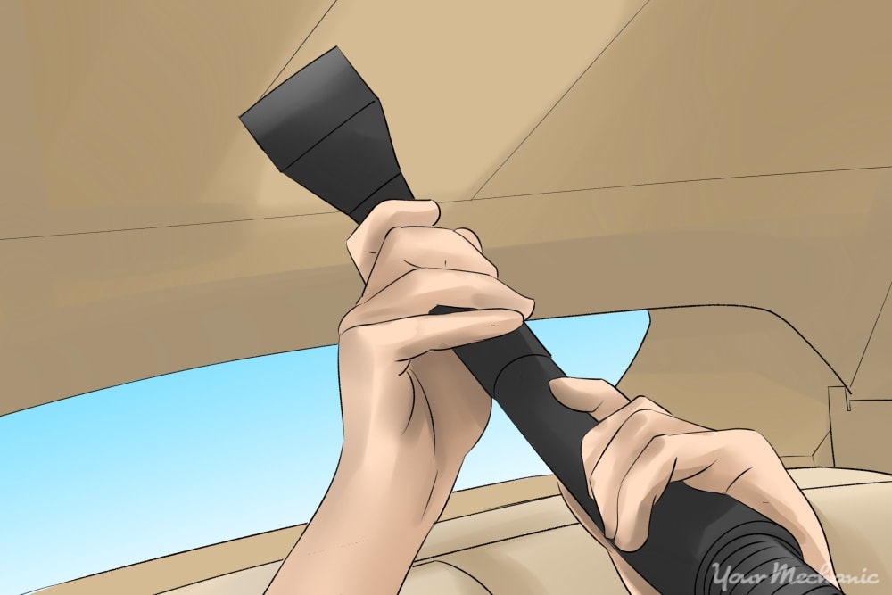 person holding hose with upholstery attachment to headliner