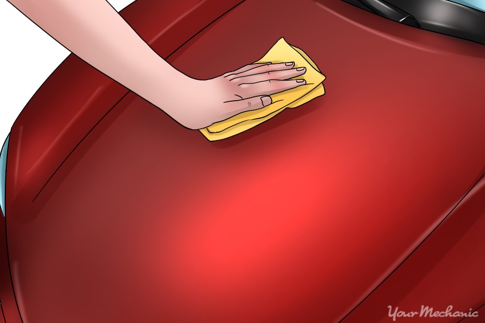 hand wiping cleaner onto car with cloth