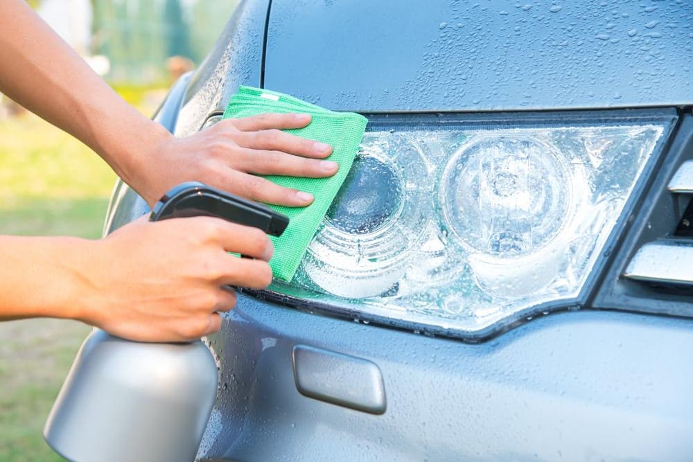 person cleaning front light with rag