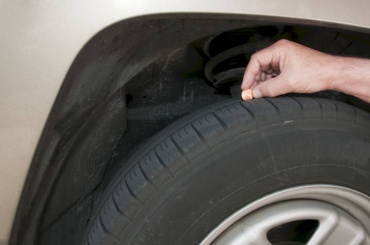 Hand holding a penny up to a tire