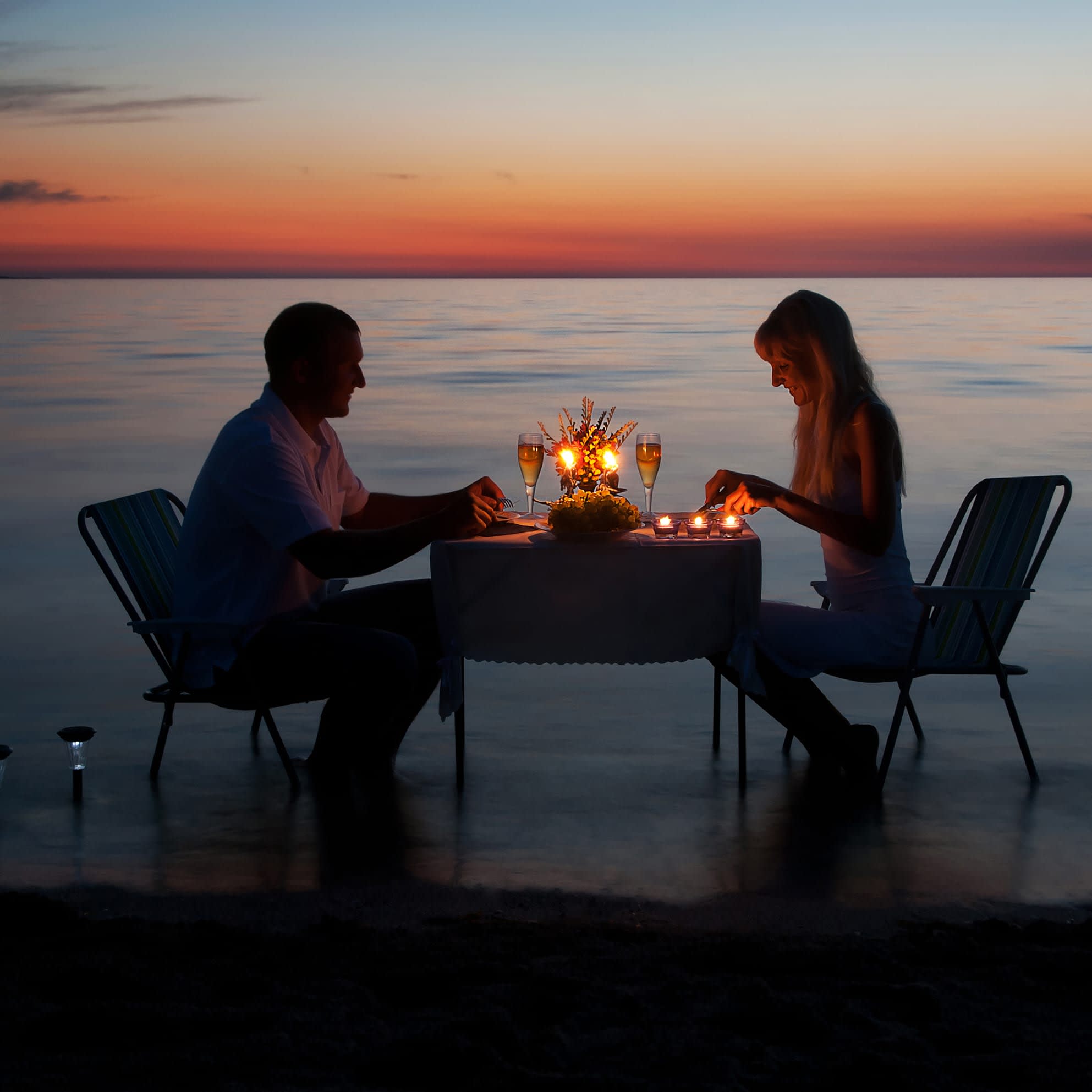 Couple enjoy a romantic meal on the beach by candlelight