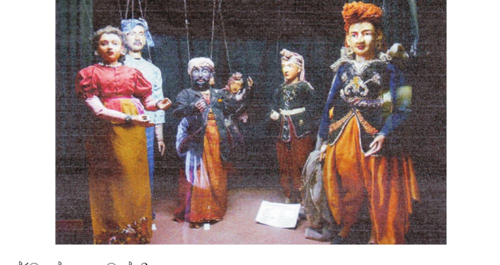 A photograph of five traditional string marionette puppets on a stage, dressed in colourful costumes, suspended by visible strings.