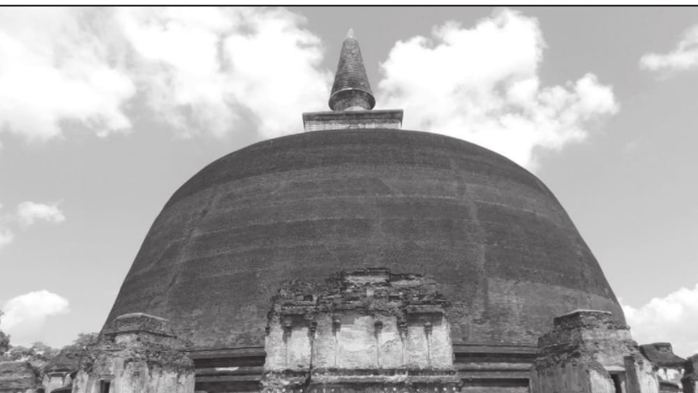 A low-angle photograph of a large brick stupa with a smooth, evenly-rounded dome and a tapering spire, partly weathered at the base.