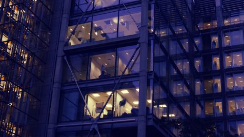 The windows of an office building at night with the silhouette of a person working late. City of London