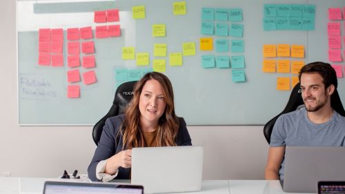 Man and woman in office with board full of postit notes behind them. Hybrid working