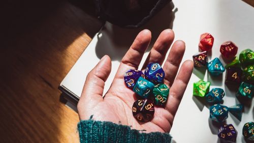 Image of a hand holding various colored and shaped role-playing dice lit by sunlight