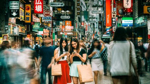 Focus on two women in a crowd of people on a busy street surrounded by prominent advertisements