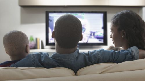 A family sits together watching an advertisement on TV