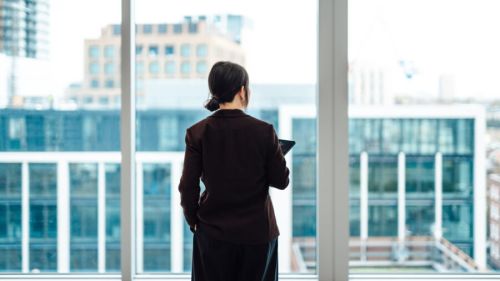 Rear view of young Asian woman in blazer, looking at city view in modern commercial building.