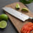 Sagenwolf Performance Santoku Knife, 18cm close up of blade on a wooden board with sliced salmon and lime 