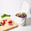 Filled OXO Good Grips Easy-Clean Compost Bin White - 2.83 L next to a chopping board with fruit and vegetables 