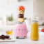 Smeg Personal Blender, 300W - Pastel Pink on the kitchen counter with blended juice and fruits