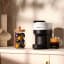 Nespresso Vertuo Pop Coffee Machine - Coconut White on the kitchen counter with a cup of coffee and capsules jar