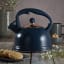 Typhoon Otto Whistling Stovetop Kettle, 1.77L - Navy Blue & Gold on the table with a mug and cookies