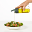 Lekue Oil Bottle, 400ml pouring oil on a salad dish