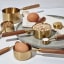 Trendz Of Today Gold & Wood Measuring Cup and Spoon Set on the kitchen counter with eggs and other ingredients