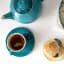 Le Creuset Cappuccino Cup and Saucer, Set of 2 -Caribbean Blue on the table with aa teapot