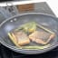 KitchenCraft Non-Stick Wire Splatter Screen, 29cm on a pan with salmon