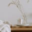 Nude Home Fragrances Lazy Sunday Wood Wick Candle, 300ml on a side table next to a bed