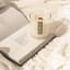 Nude Home Fragrances Beach House Wood Wick Candle, 300ml on a book on a bed