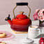 Le Creuset Classic Whistling Stovetop Kettle with Heart Knob, 1.6L - Cerise on the table with tea cups