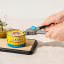 Dreamfarm Dopener 3-in-1 Ergonomic Can Opener opening a can on a chopping board