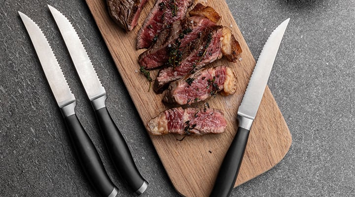 Serrated steak knives on a board with steak