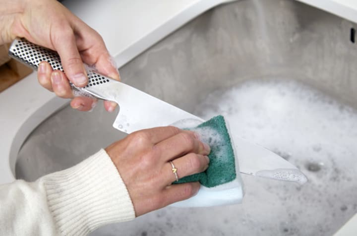 Person washing knife with sponge