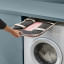 Joseph Joseph Hold-All Peach Collapsible Laundry Basket, 35L stored between the washing machine and shelf